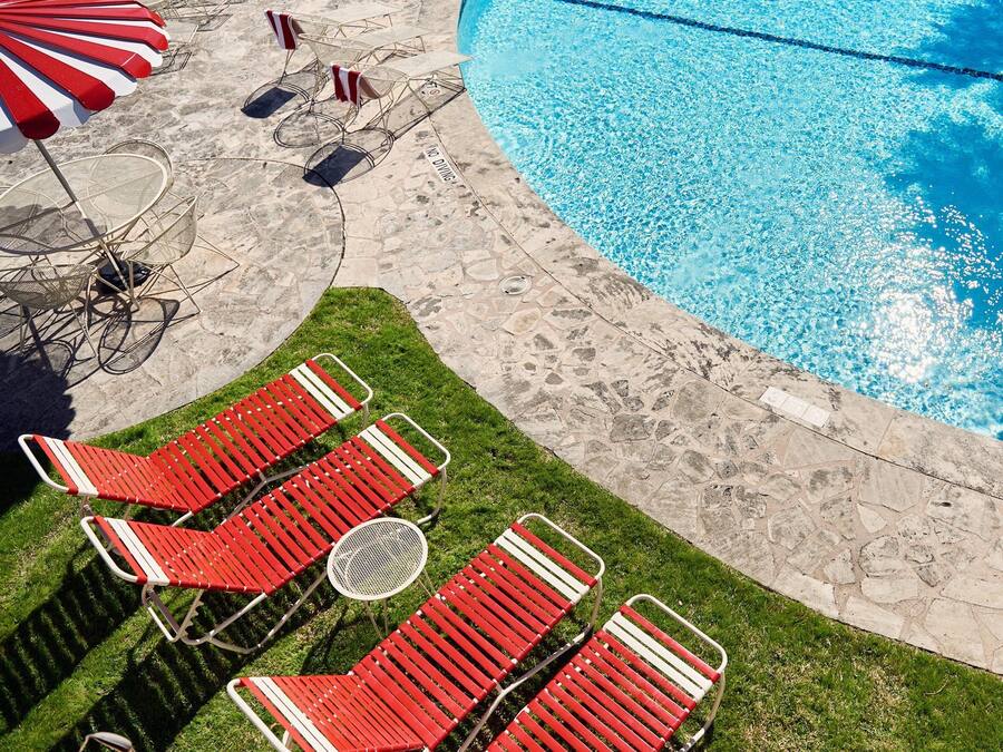 Una piscina con plataforma de piedra, sillas de descanso rojas y blancas, y un letrero de prohibido bucear.
