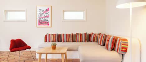 A modern living room with a white sofa, colorful striped pillows, a red chair, a wooden table, and a floor with hexagonal tiles.