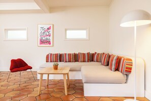A modern living room with a white sofa, colorful striped pillows, a red chair, a wooden table, and a floor with hexagonal tiles.