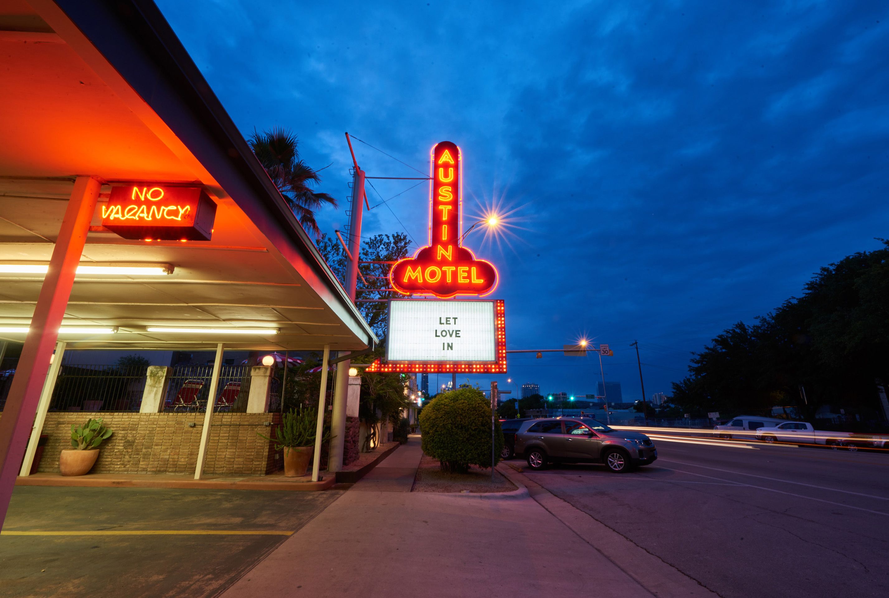 A motel with neon signs, a 'NO VACANCY' sign, and a 'LET LOVE IN' sign.