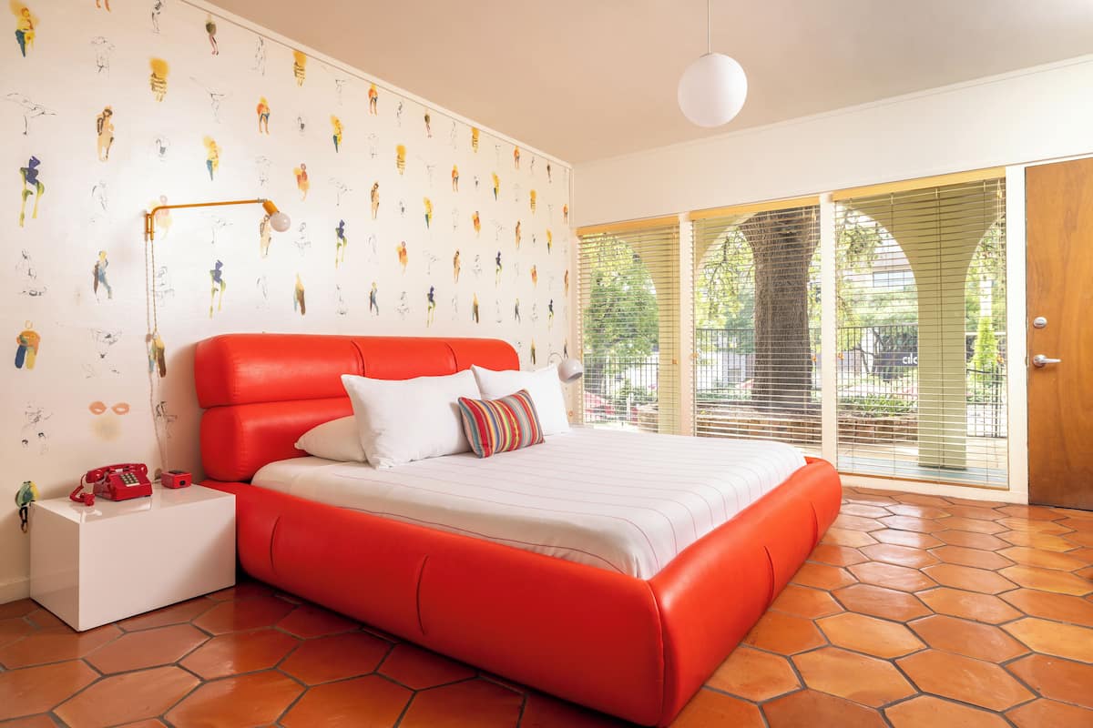 A modern bedroom with a red bed, white bedding, a white nightstand, and a red telephone.
