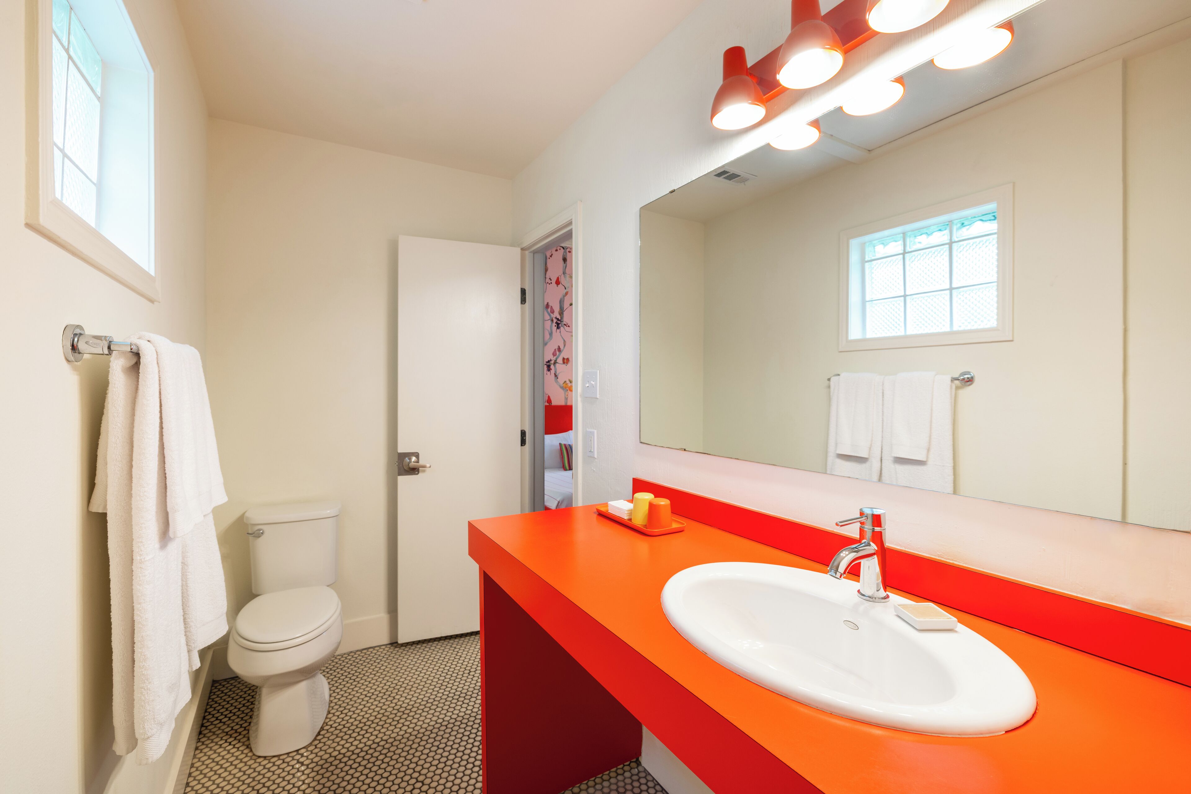 Un bany amb vàter blanc, un lavabo taronja i un mirall gran.