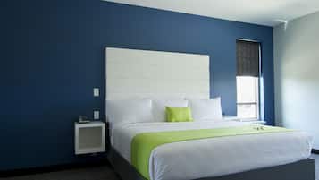 Een moderne hotelkamer met een groot bed, witte beddengoed, een groene plaid en een klein nachtkastje met een telefoon.