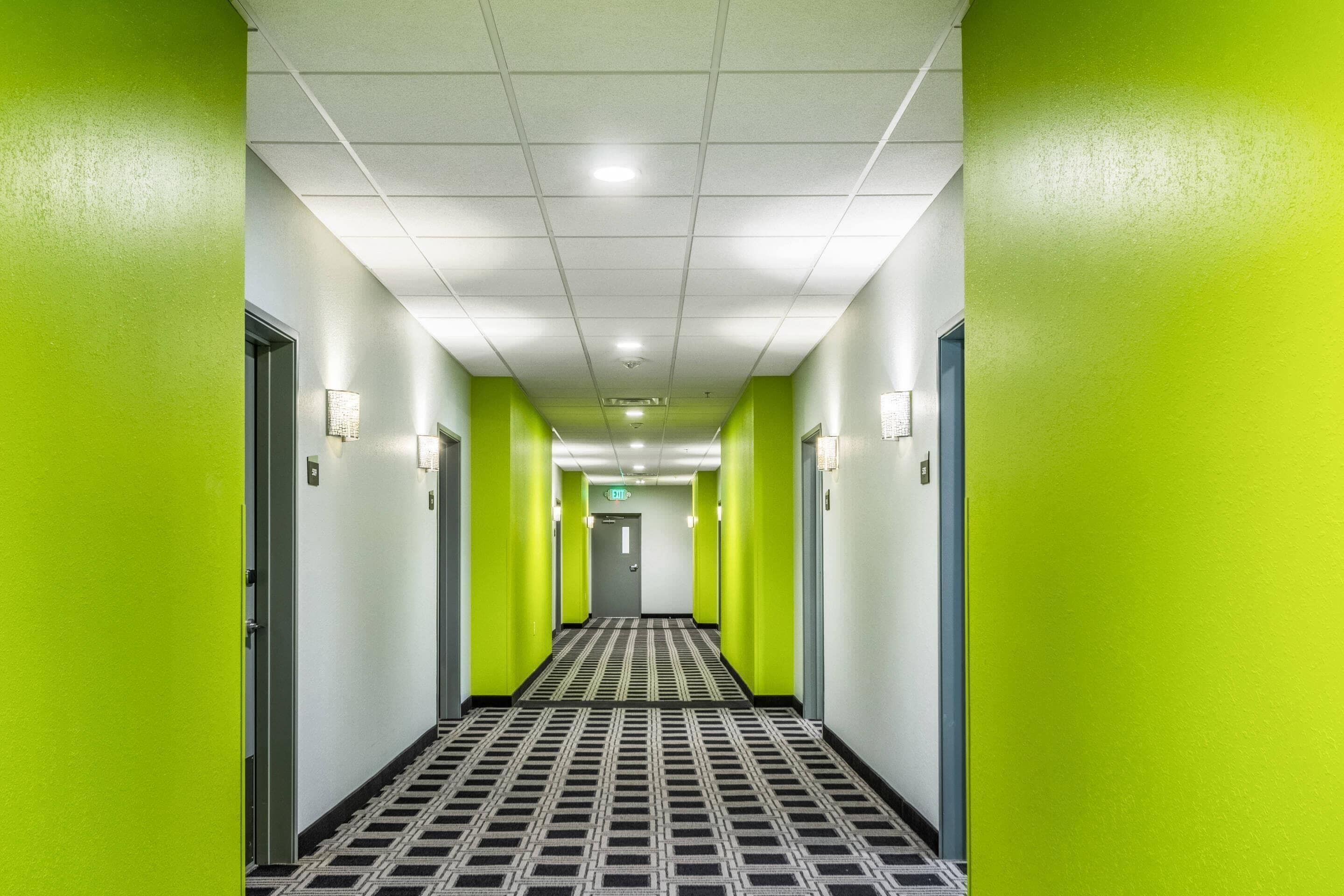 A hotel hallway with green walls, a patterned floor, and a ceiling with recessed lighting.