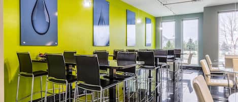 A modern restaurant with high tables and chairs, bright green walls, and large windows.