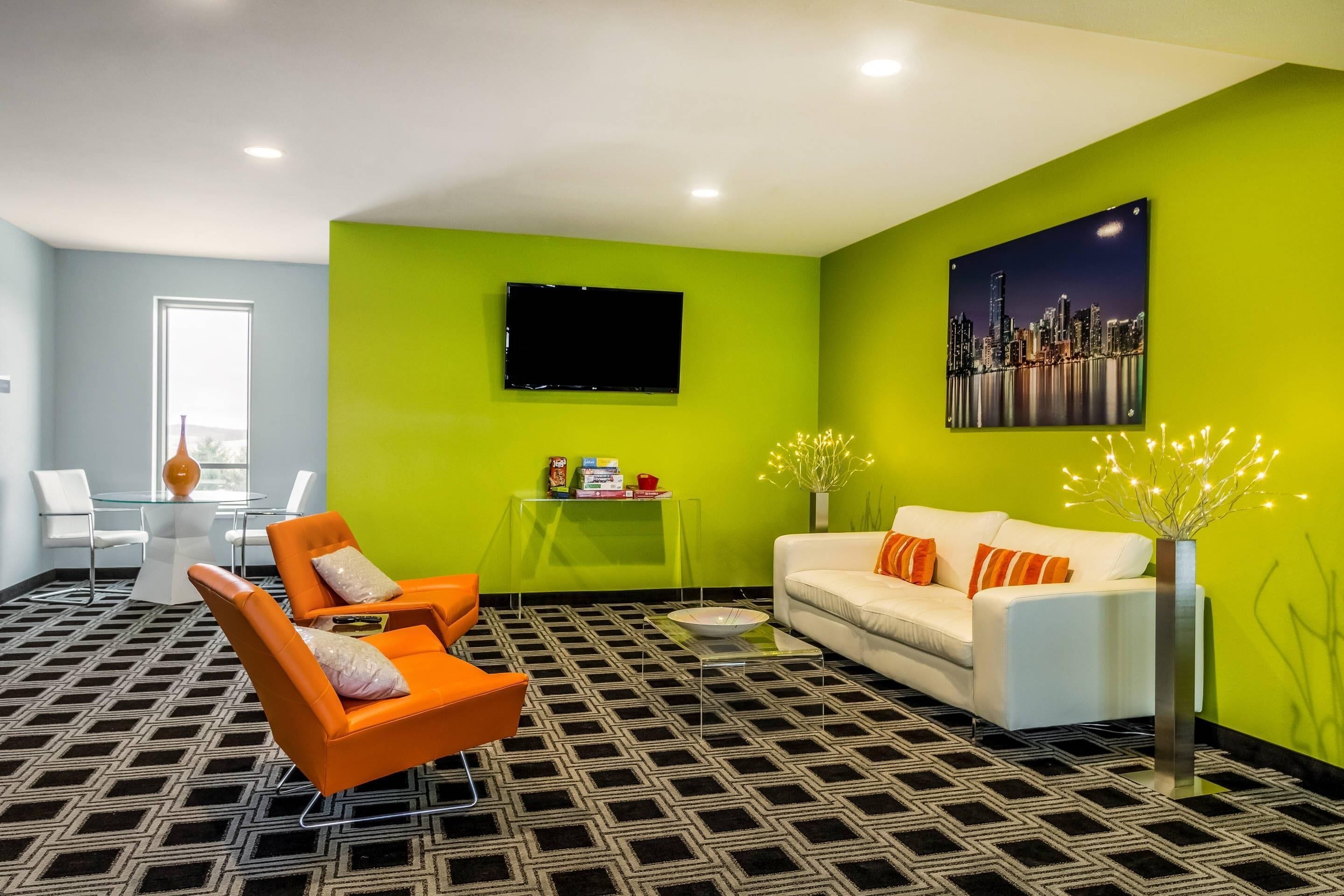 A modern living room with a sofa, two armchairs, a glass coffee table, a flat-screen TV, and a cityscape painting.