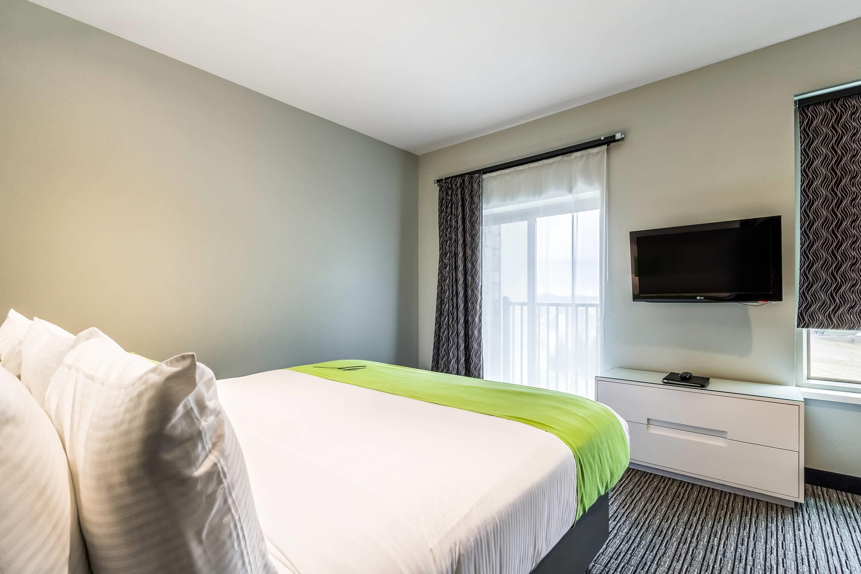Une chambre d’hôtel avec un lit, une télévision, une fenêtre avec des rideaux et un bureau.