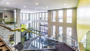 Un intérieur moderne avec un escalier en verre, de grandes fenêtres et un plafond haut.