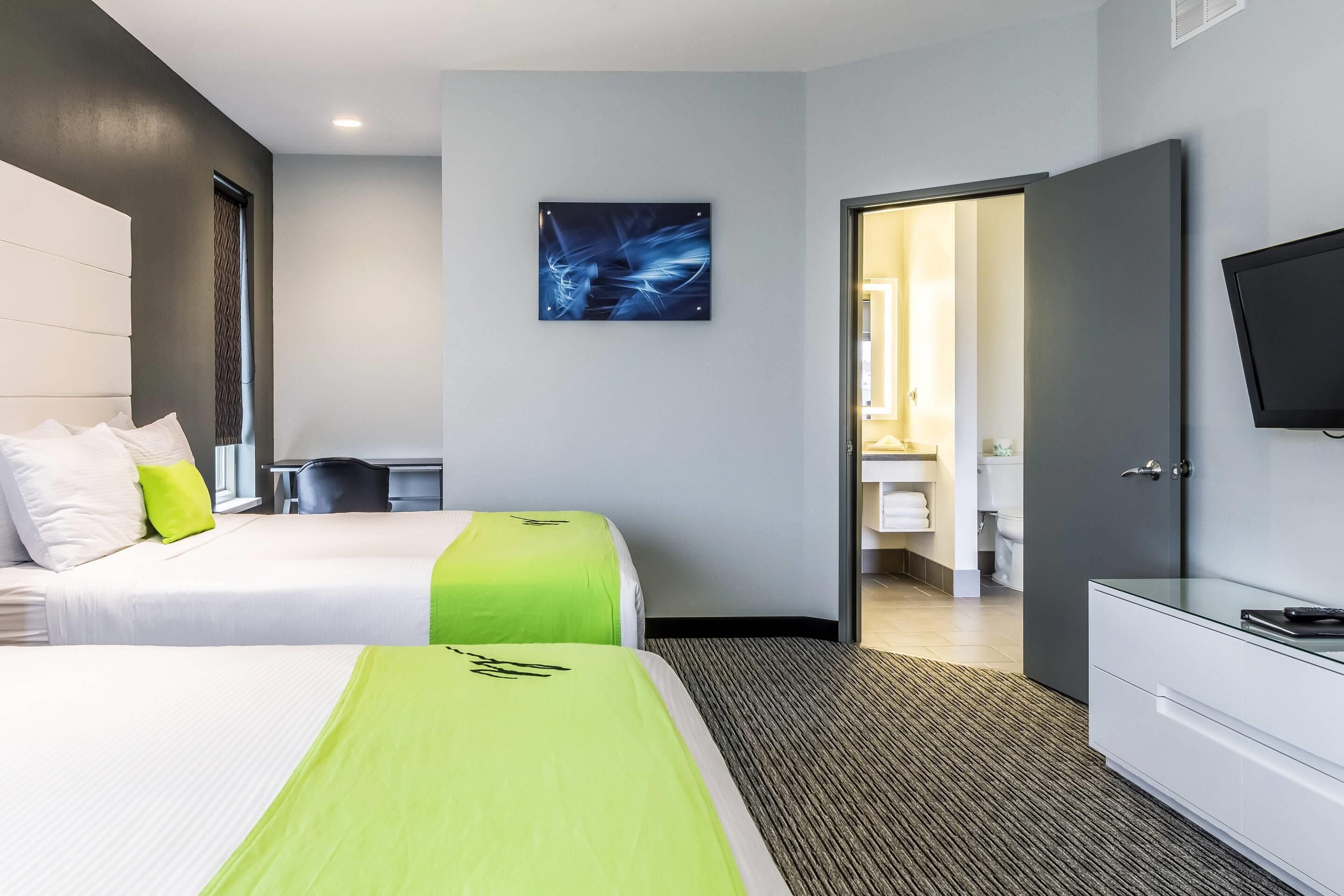 Een hotelkamer met twee bedden, een bureau, een televisie en een badkamer die door een geopende deur zichtbaar is.