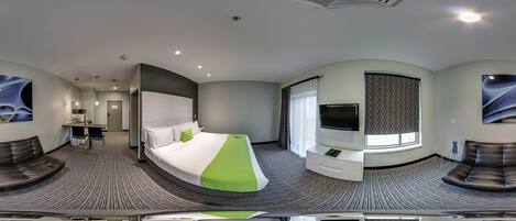 Una camera d'albergo moderna con un letto a forma di ferro di cavallo, una TV a schermo piatto, una scrivania e un'area salotto con un divano e poltrone.