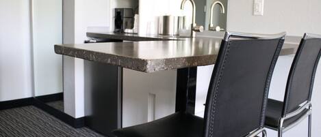 Una cocina moderna con electrodomésticos de acero inoxidable, encimera de granito y sillas de cuero negro.
