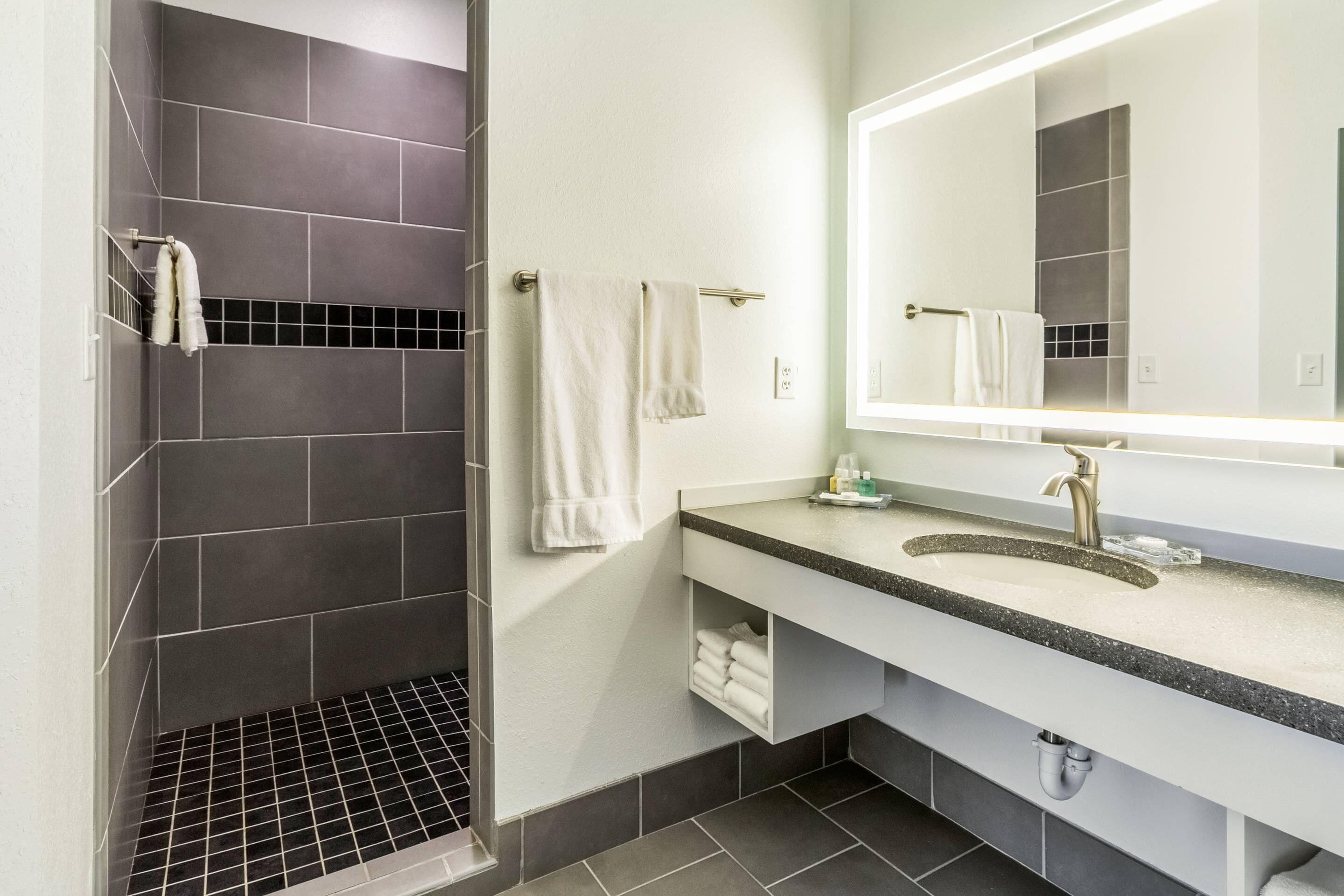 Un baño moderno con ducha, lavamanos con espejo y un perchero para toallas.