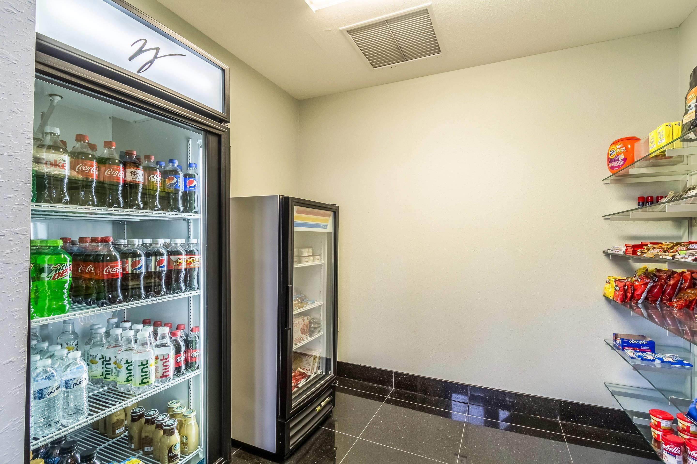 Et hotelværelse med minibar fyldt med drikkevarer og snacks, et køleskab og et flisegulv.