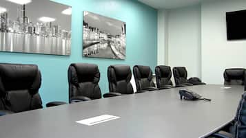 A conference room with a long table, six black leather chairs, two black and white photographs on the wall, and a flat-screen TV mounted on the wall.
