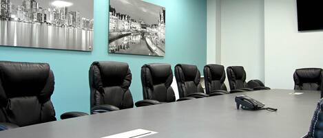 A conference room with a long table, six black leather chairs, two black and white photographs on the wall, and a flat-screen TV mounted on the wall.