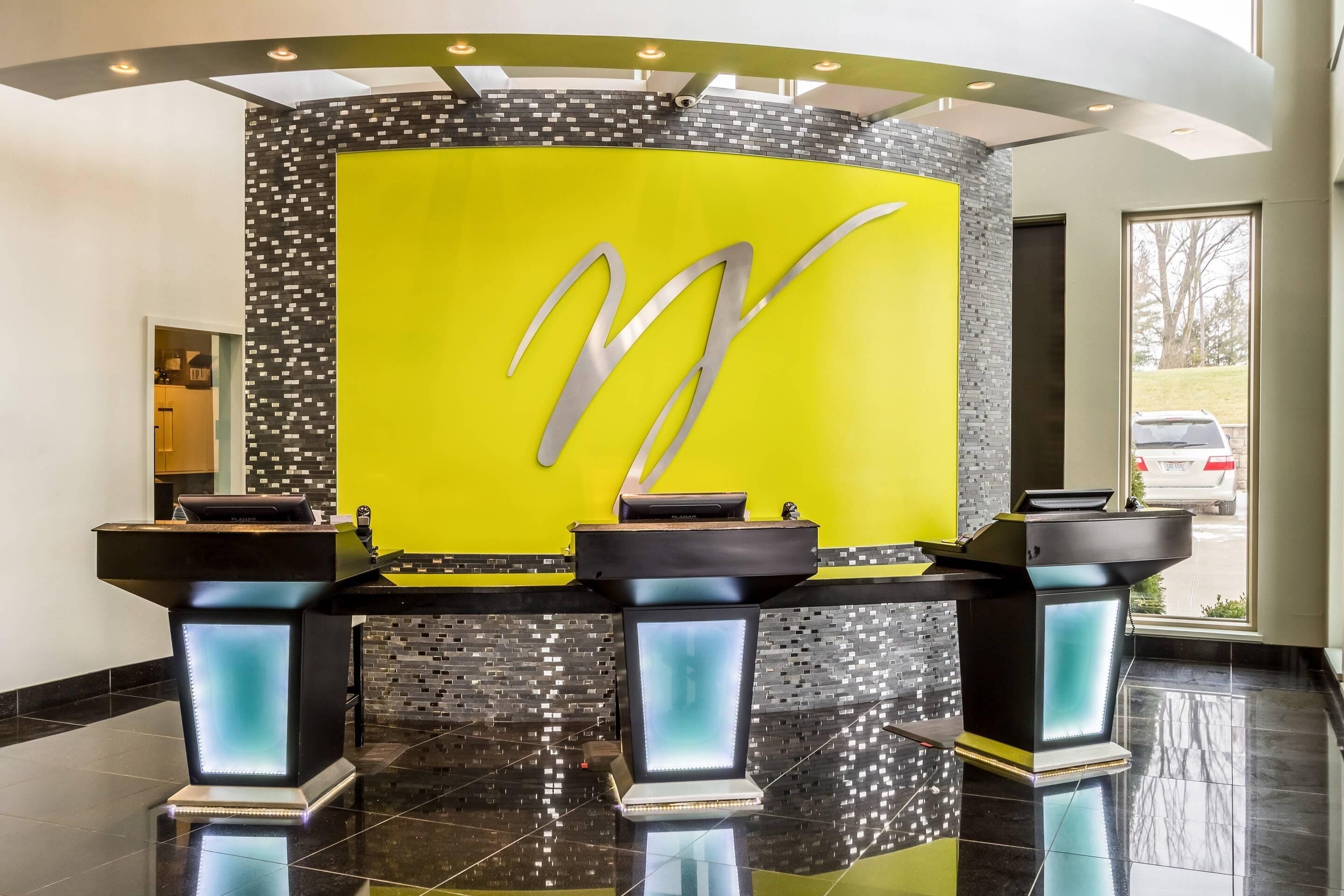 A reception area with a bright yellow wall, a large metallic 'W' logo, and three black podiums with illuminated bases.