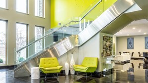 Un hall d’entrée moderne avec un escalier, des rampes en verre et des fauteuils d’un vert vif.