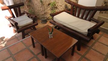 A wooden bench with a cushion, a small table with a plant, and a potted plant against a textured wall.