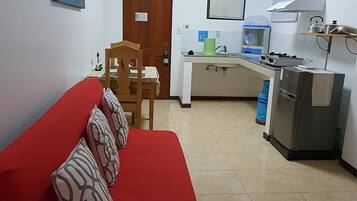 A compact living space with a red sofa, a wooden dining table, and a kitchenette.