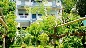 Un edificio de varios pisos con balcones, rodeado de abundante vegetación y plantas en macetas.