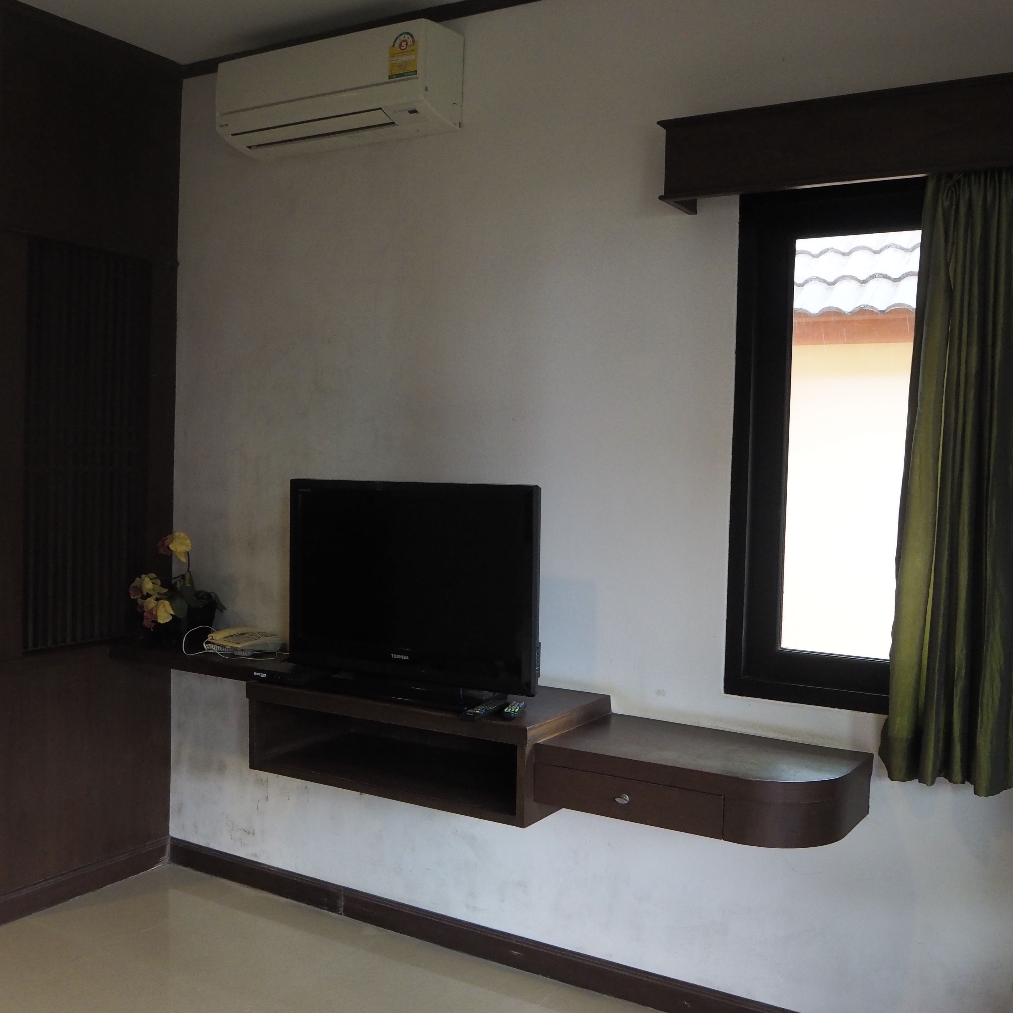 A living room with a flat-screen TV on a stand, a small table with a telephone, and a window with curtains.