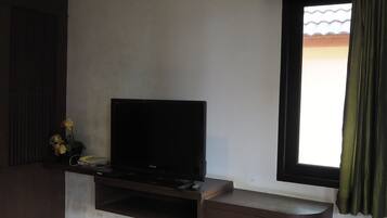 A living room with a flat-screen TV on a stand, a small table with a telephone, and a window with curtains.