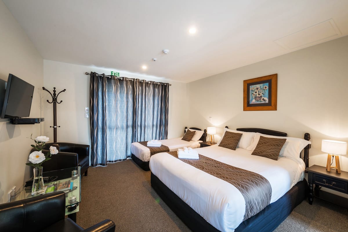 A hotel room with two beds, a desk with a chair, a television, and a coat rack.