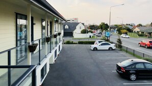A motel with a parking lot, a road with cars, and a building in the background. - 123 Motel (Christchurch)