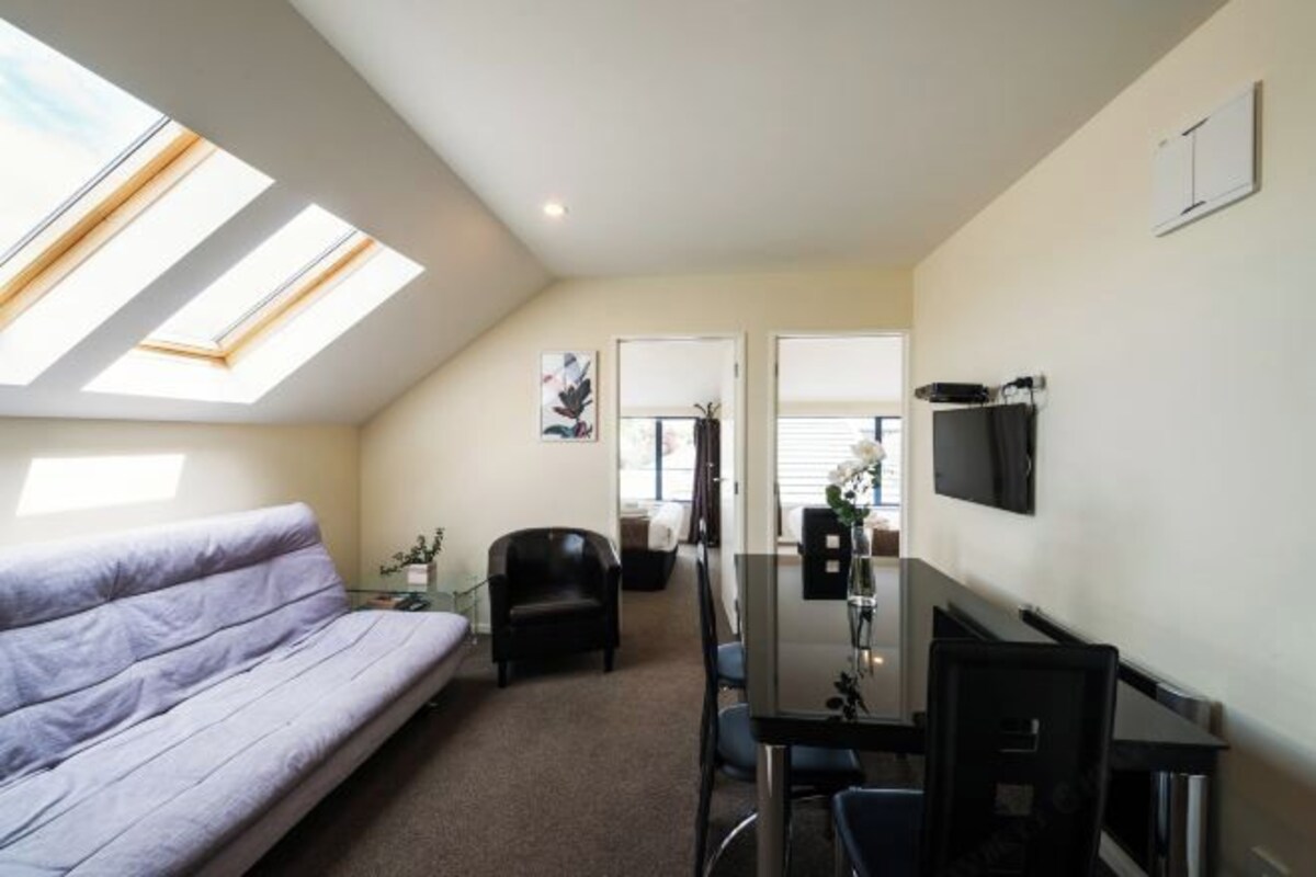 Un espacio habitable compacto con sofá, mesa de comedor y televisión. Cuenta con tragaluces que proporcionan luz natural.