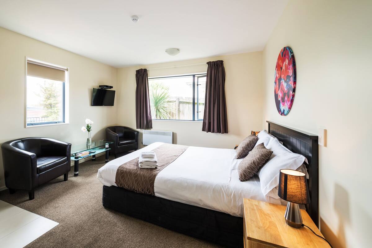 A hotel room with a bed, a desk, a chair, a TV, and a window.