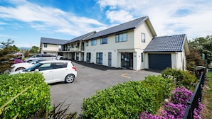 A multi-story residential building with a parking area and lush greenery. - 123 Motel (Christchurch)