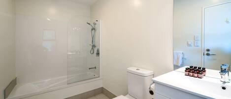 Un baño moderno con ducha de vidrio, inodoro blanco y tocador con artículos de aseo.