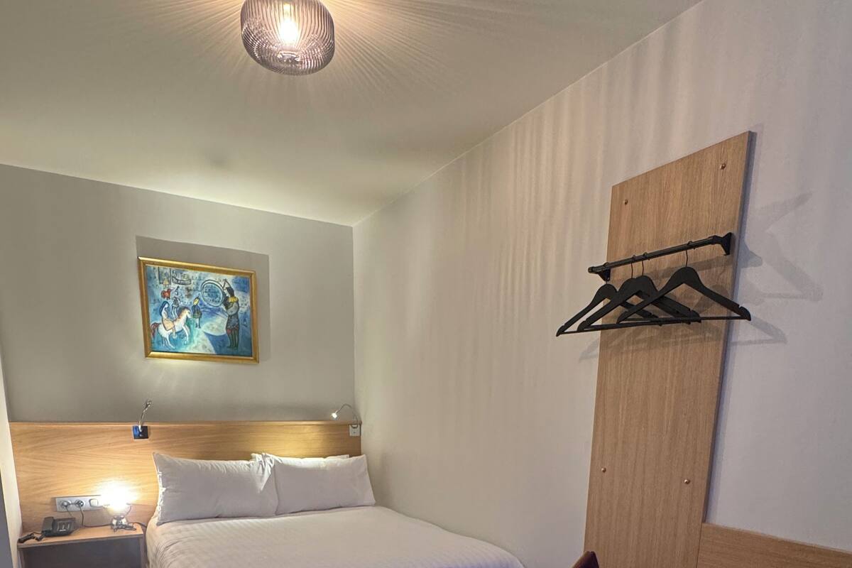 Habitación de hotel con cama de madera, mesita de noche, lámpara y un escritorio con silla.
