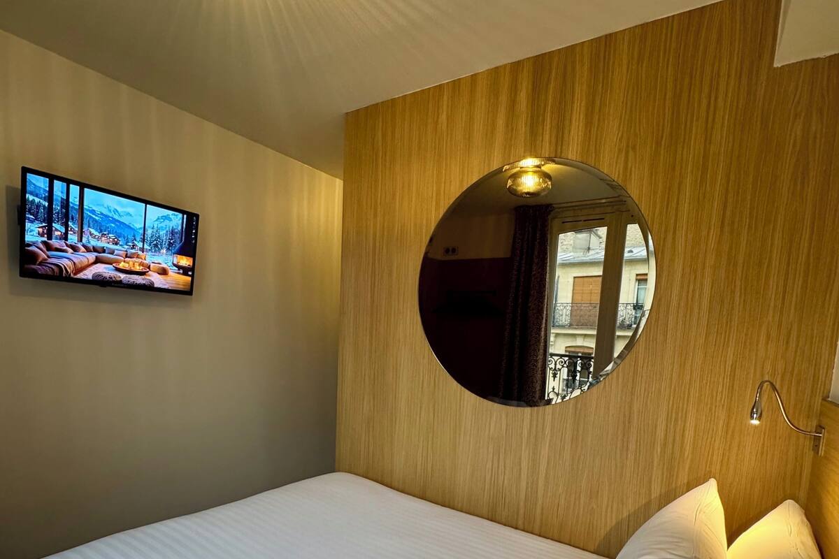 Una habitación de hotel con una cama grande, un espejo redondo, un televisor de pantalla plana y una lámpara en el techo.