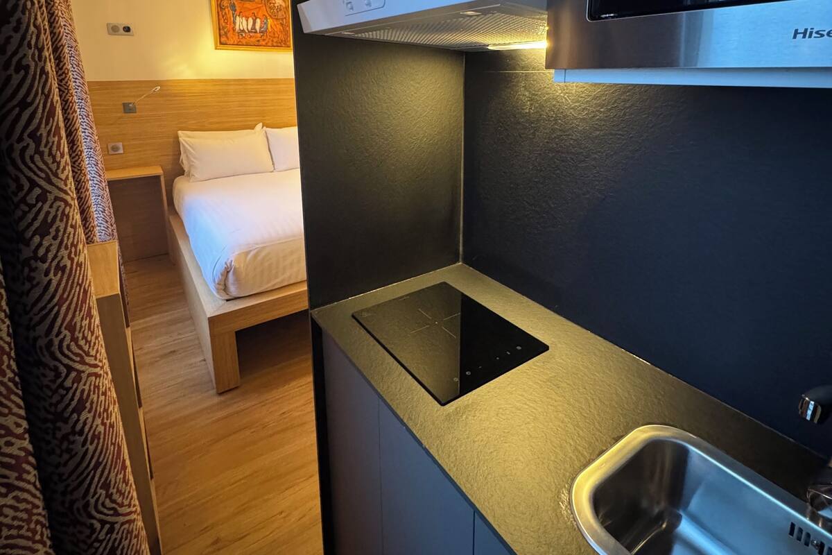 Una kitchenette compacta con microondas integrado, un lavaplatos de acero inoxidable y una cama en la habitación contigua.