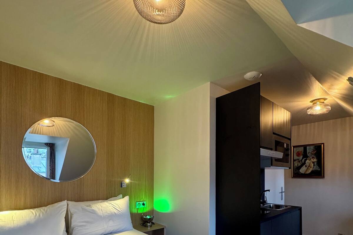 Un dormitorio moderno con una cama grande, un espejo redondo y una pequeña kitchenette.