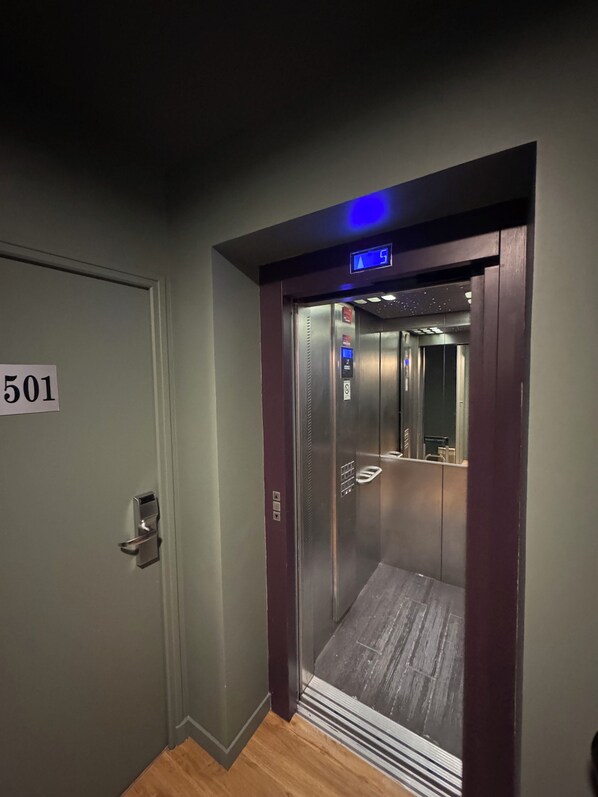 Un ascensor con pantalla digital, una puerta con el símbolo del número y suelo de madera.