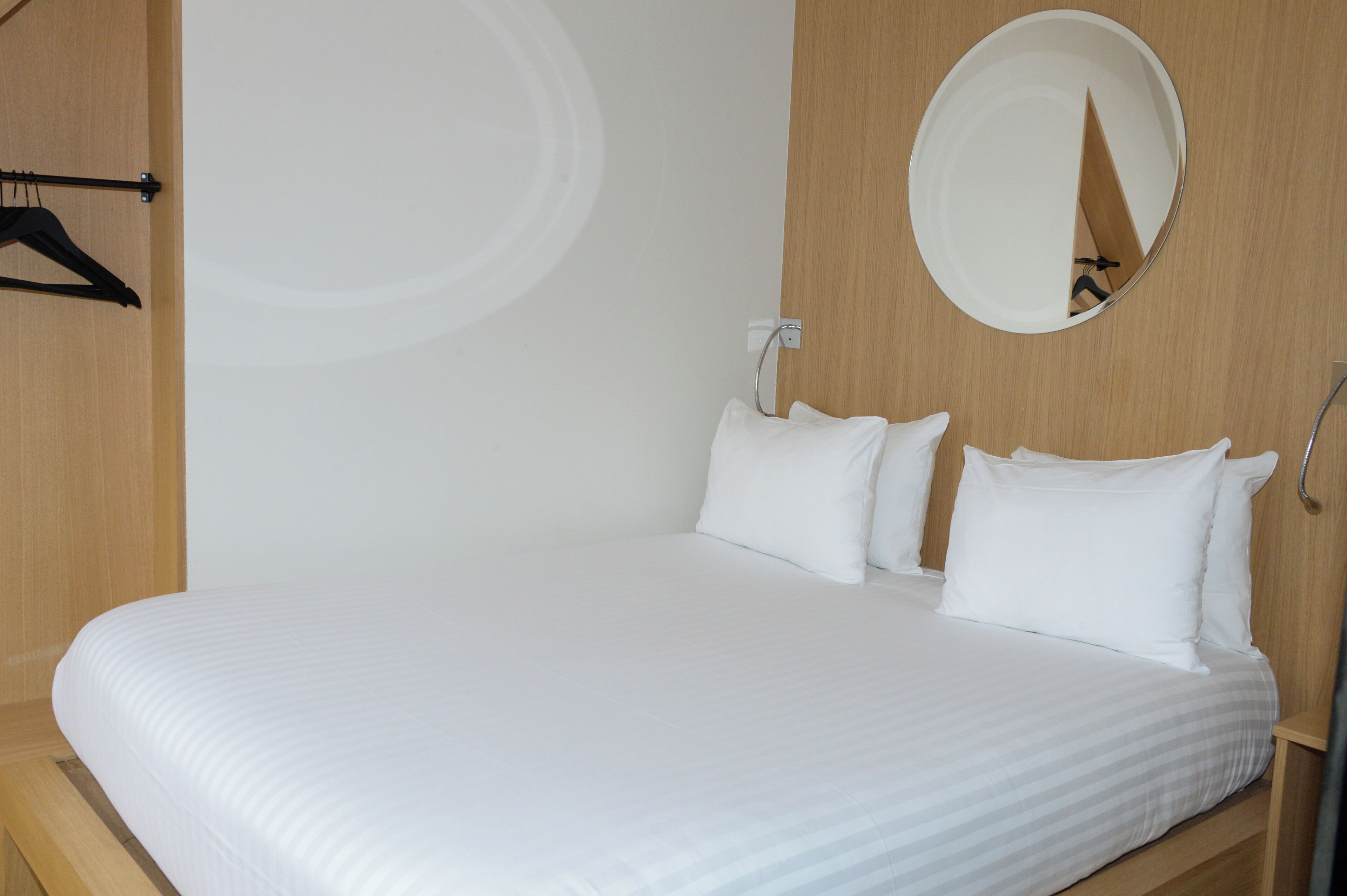 A neatly made bed with white linens in a room with wooden walls and a round mirror on the wall.