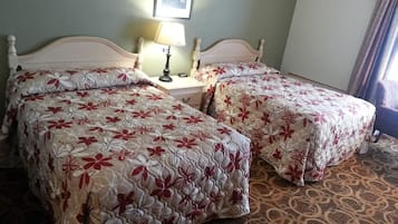 Ein Zimmer mit zwei Betten, einem Nachttisch mit Lampe, einem gerahmten Bild an der Wand und einem gemusterten Teppich.