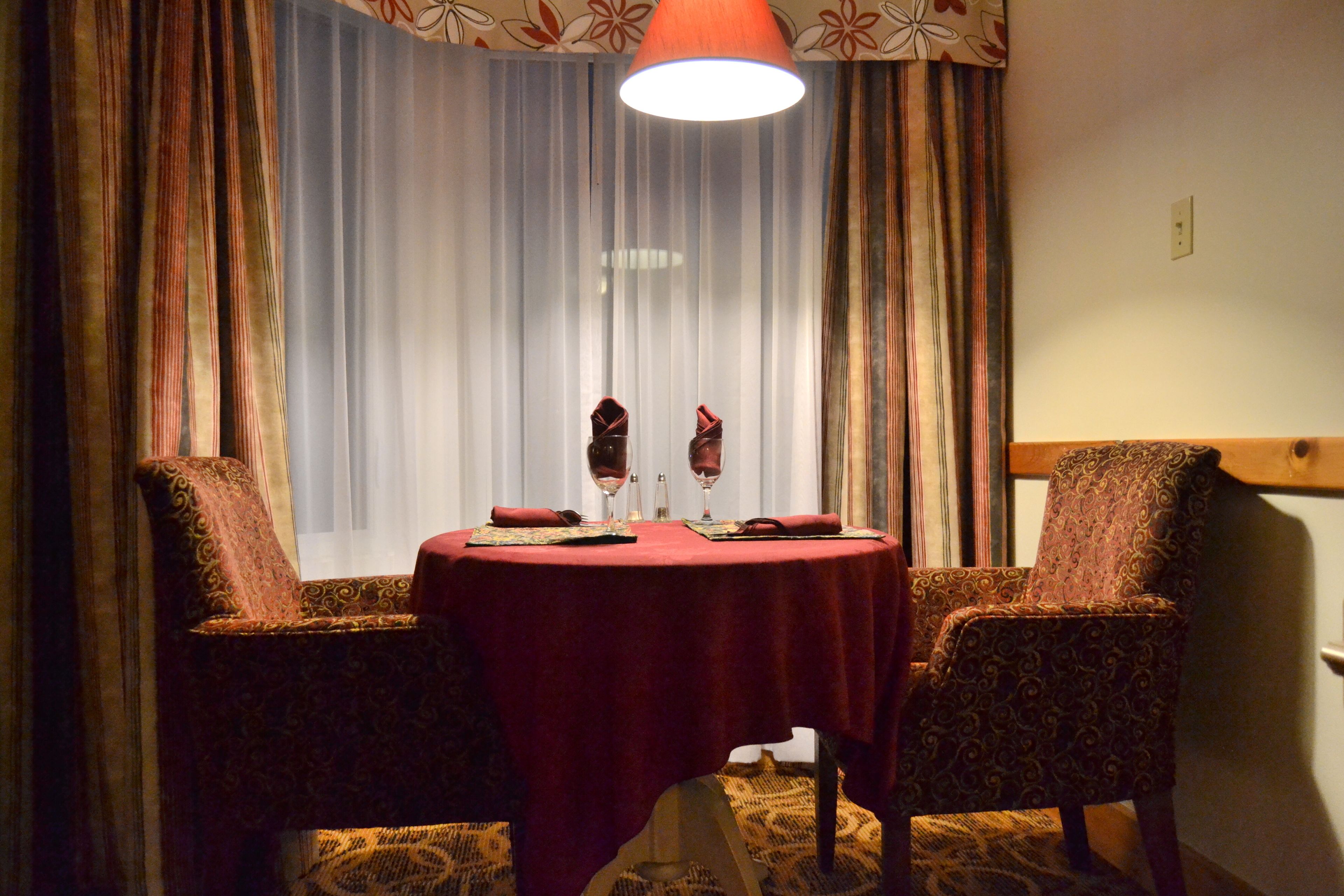 A dining area with a round table, two patterned chairs, a red tablecloth, and a pendant light.