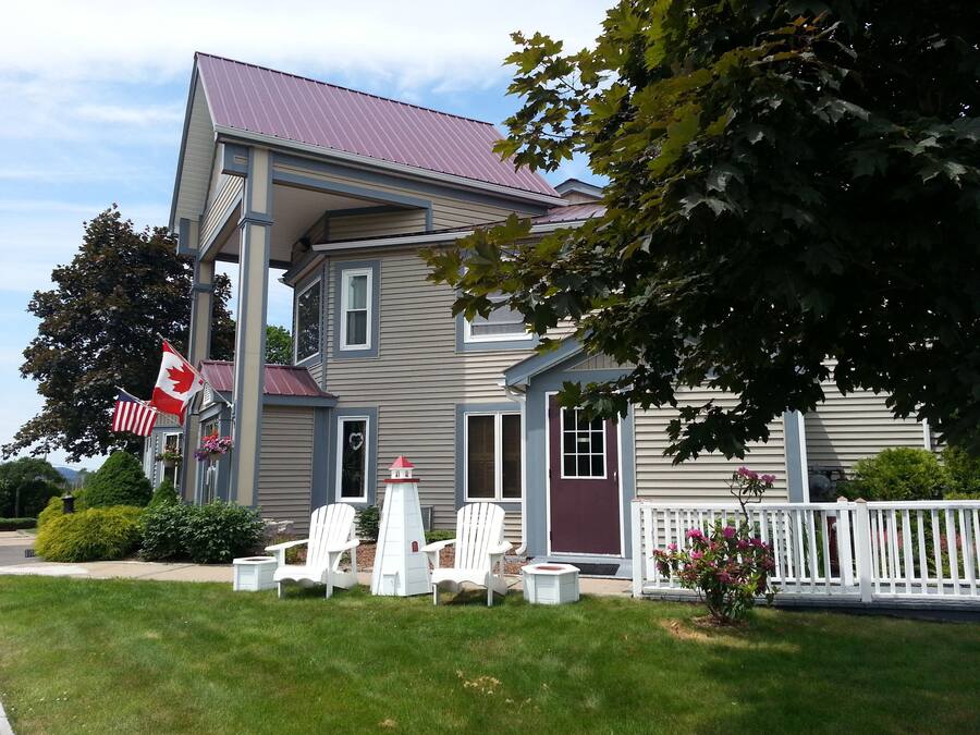 A two-story house with a red roof, a porch with white chairs, and a Canadian flag.