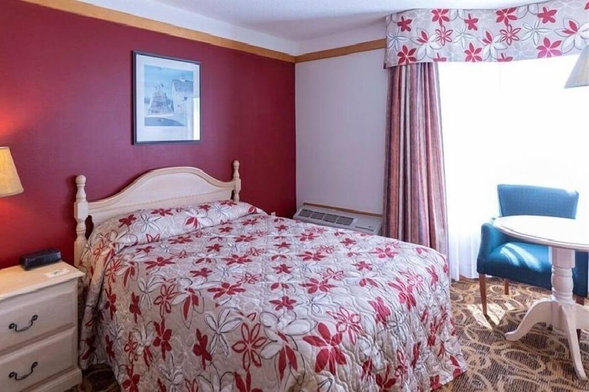 A hotel room with a bed, a desk, a chair, and a window with curtains.