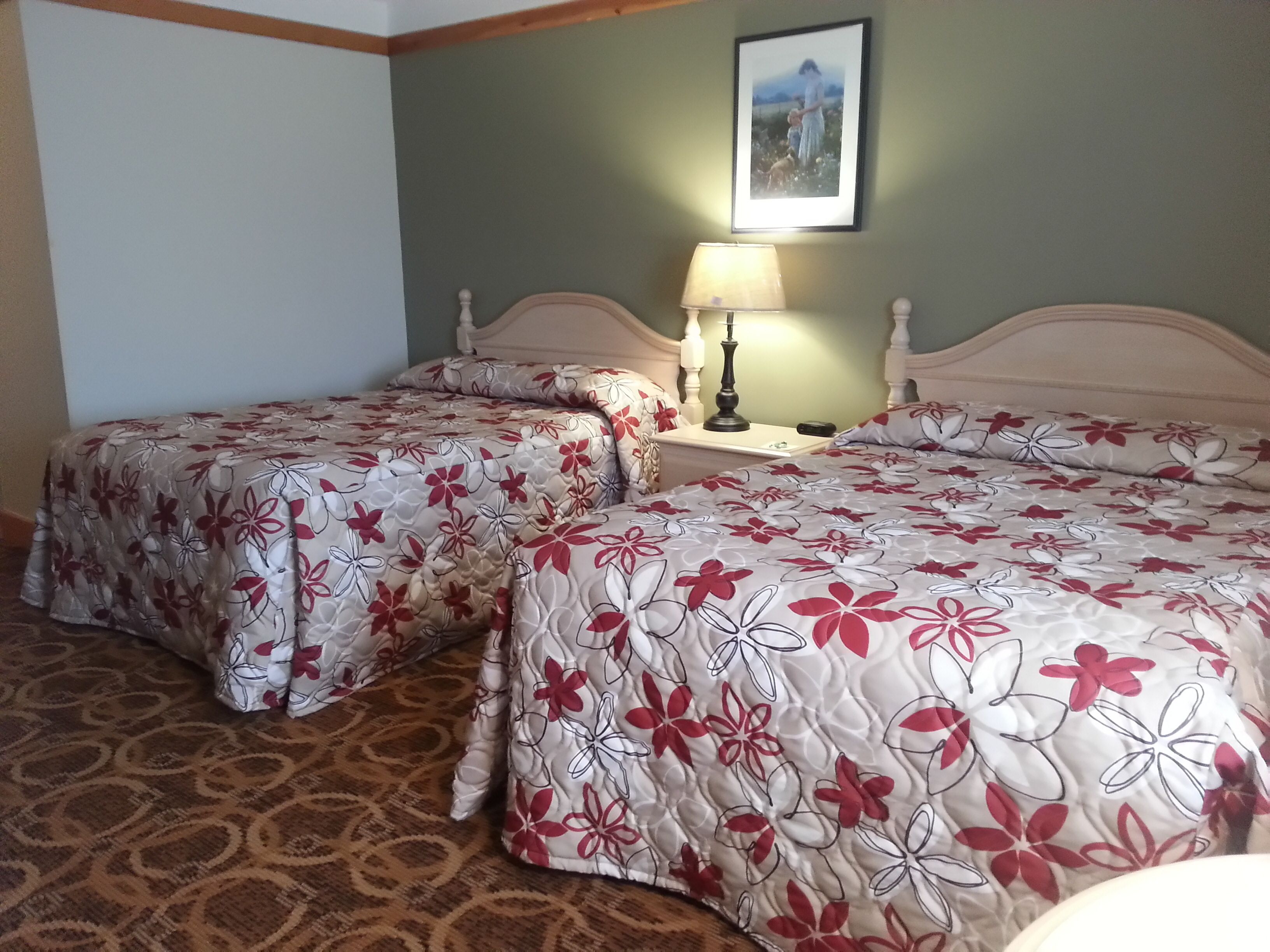 Une chambre d’hôtel avec deux lits, une table de chevet avec une lampe et un tableau encadré au mur.