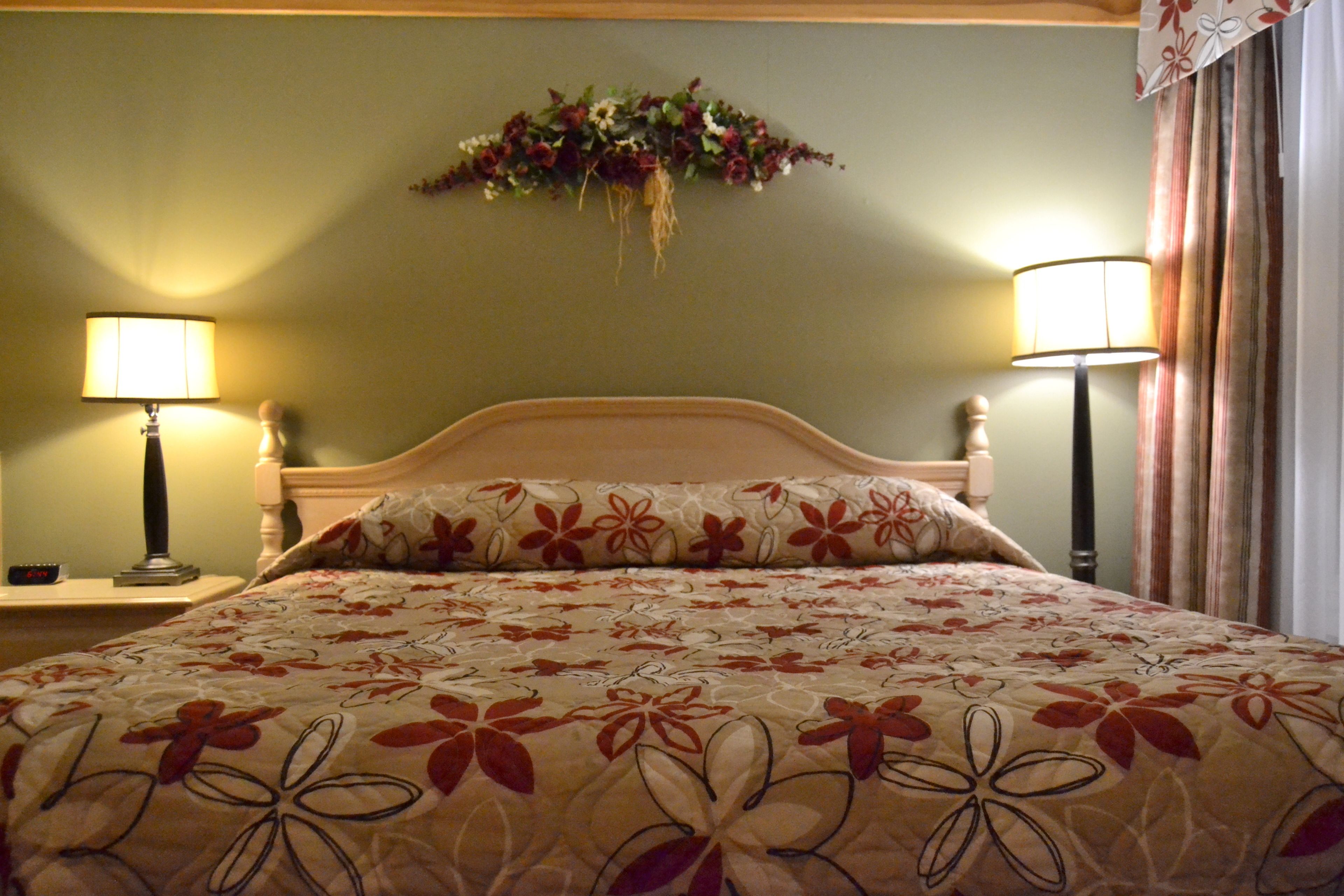 A hotel room with a bed, two bedside lamps, a floral wall decoration, and a curtain.
