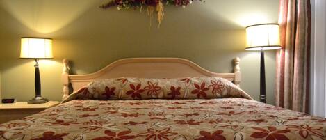 A hotel room with a bed, two bedside lamps, a floral wall decoration, and a curtain.