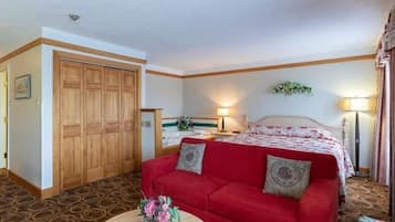 Une suite comprenant un grand lit, un canapé rouge, une armoire en bois, une salle de bain avec baignoire et une petite table ronde agrémentée d’un vase de fleurs.