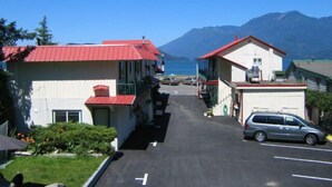 A row of buildings with red roofs, a parking area, and a view of the sea and mountains in the background. - Harrison Spa Motel (Harrison Hot Springs)
