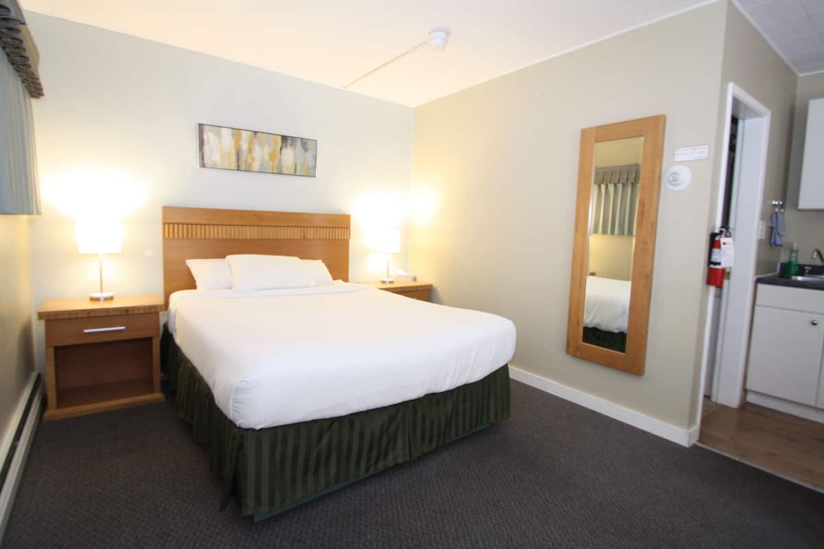 A hotel room with a large bed, two bedside tables with lamps, a mirror, and a small kitchenette.