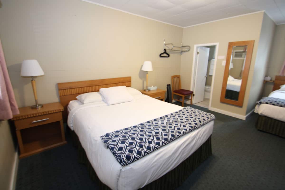 A hotel room with a large bed, bedside tables, a chair, a mirror, and a door leading to a bathroom.