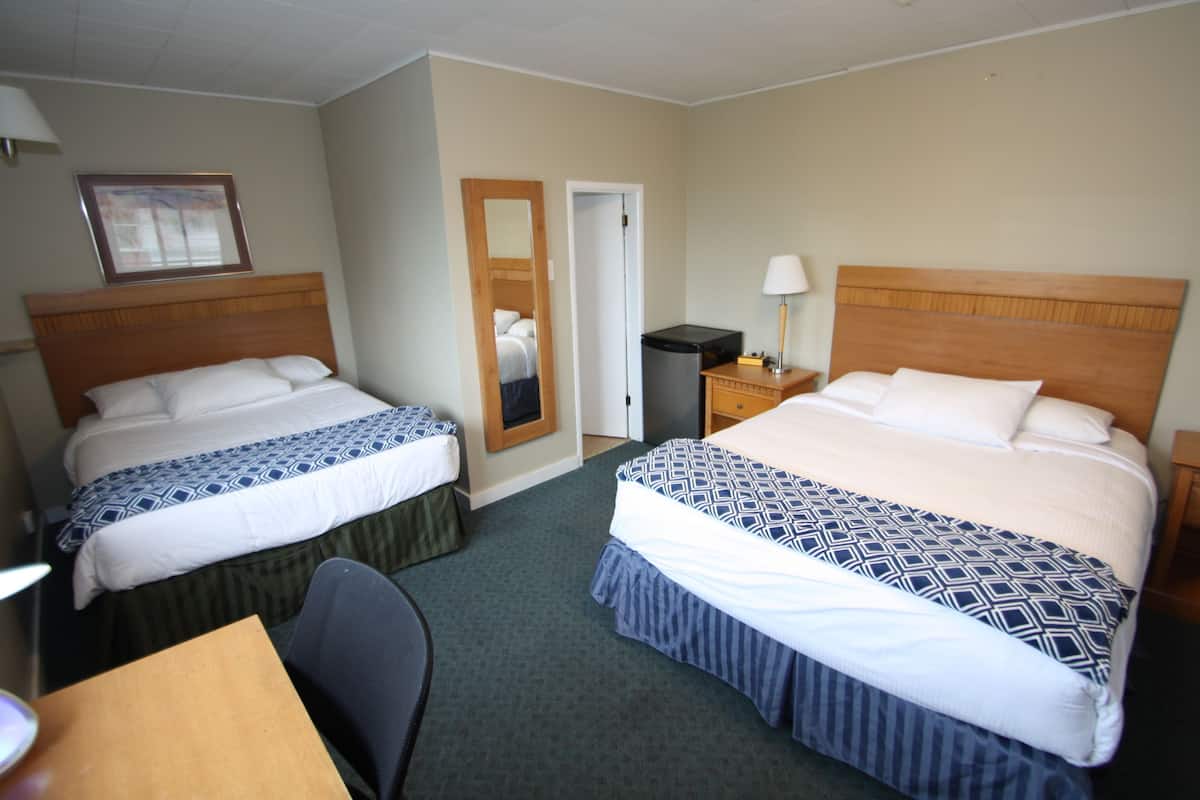 A hotel room with two beds, a desk, a chair, a mirror, and a nightstand with a lamp.